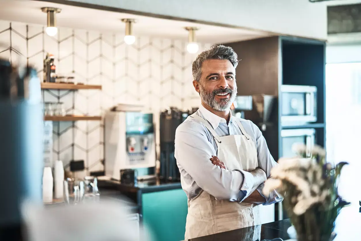 Smiling small business owner with folded arms in a modern restaurant, showcasing a successful and welcoming business environment.